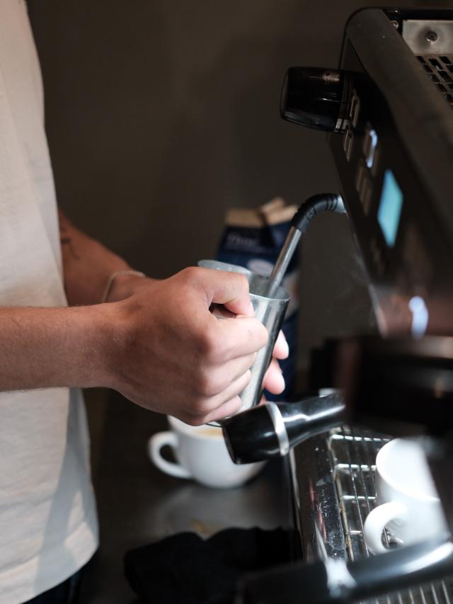 Der steames mælk i en stålkande fra en espressomaskine