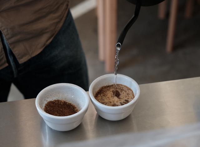 Gennem en tynd svanehals hældes vand ned i kopper med kaffebønner i