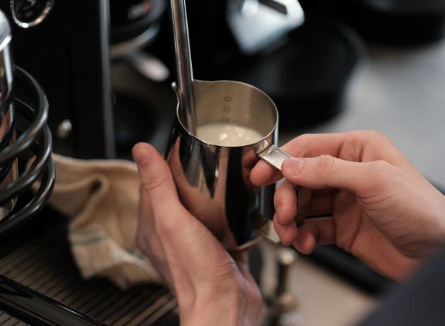 Mælk steames i en lille stålkande der holdes af to hænder