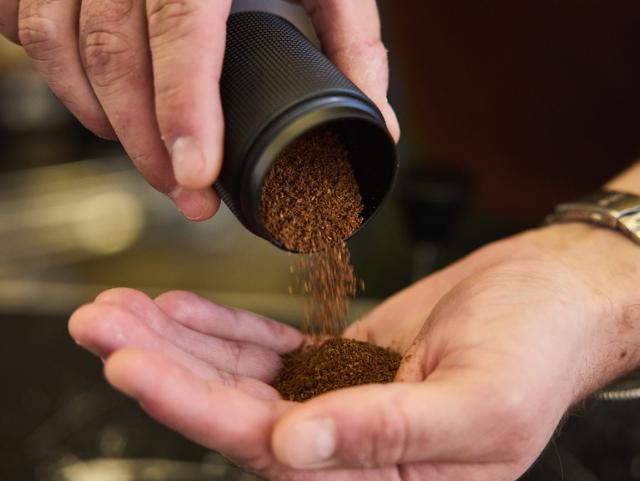 Formalede kaffebønner hældes fra en sort beholder og ned i en håndflade