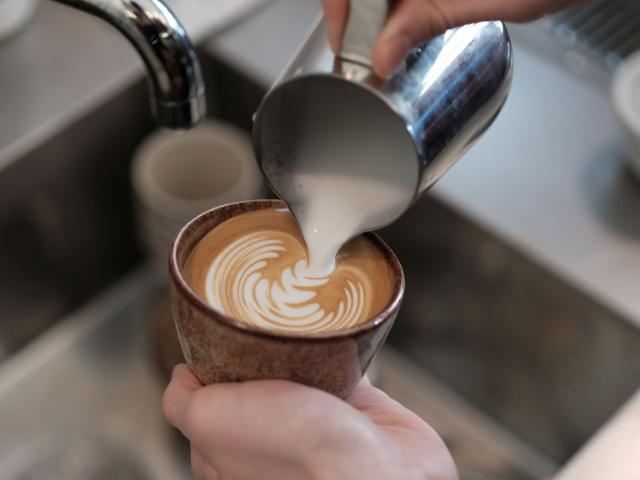 Der hældes mælk fra en steamkande ned i en cappuccino så det danner et flot mønster