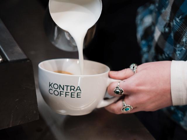 Steamet mælk hældes ned i en hvid kop med KONTRA Coffee logo