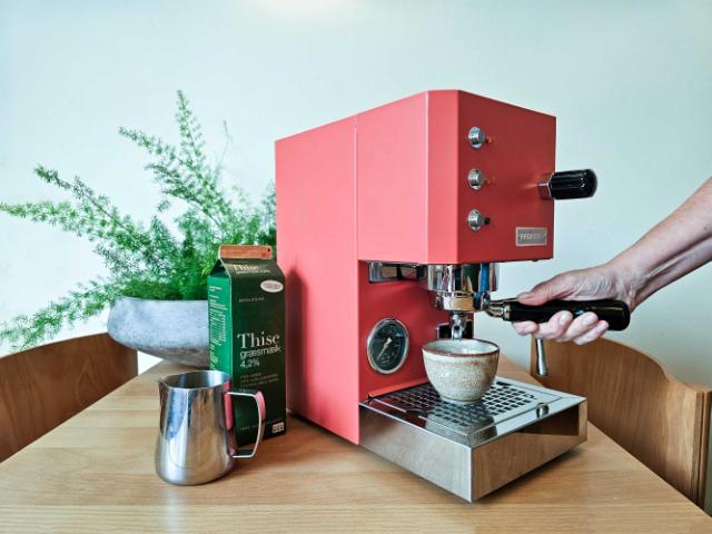 Pink profitec espressomaskine står på et bord sammen med en liter mælk og en steamekande