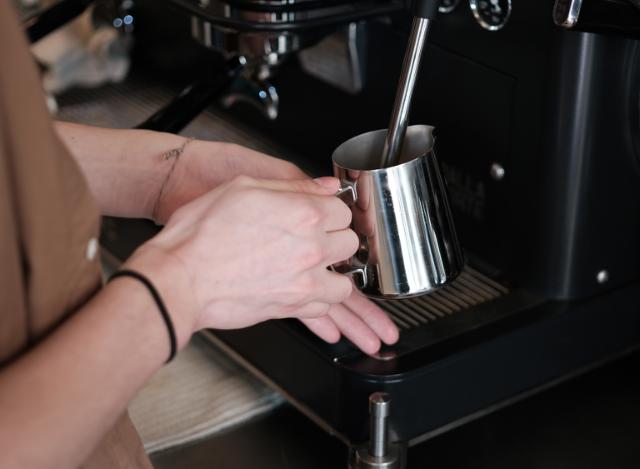 Barista steamer mælk i en stålkande på en espressomaskine fra Dalla Corte