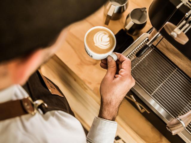 Barista har brygget eb kop kaffe med latteart i toppen