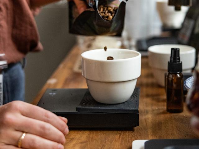 Kaffeboenner hældes ned i en hvid skål, der står paa en kaffevægt