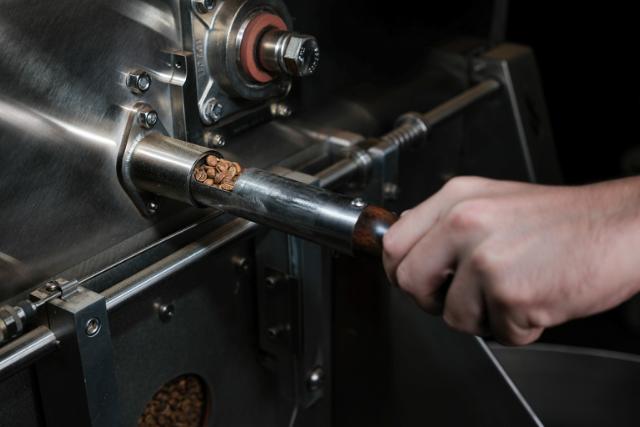 Hånd trækker samplespoon ud af kafferister for at se hvordan bønnerne har det