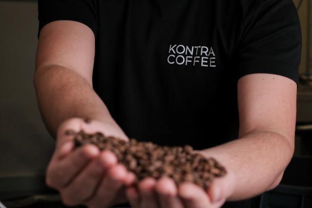 To håndfulde kaffe holdes frem mod kameraet. I baggrunden ses et KONTRA COFFEE-logo