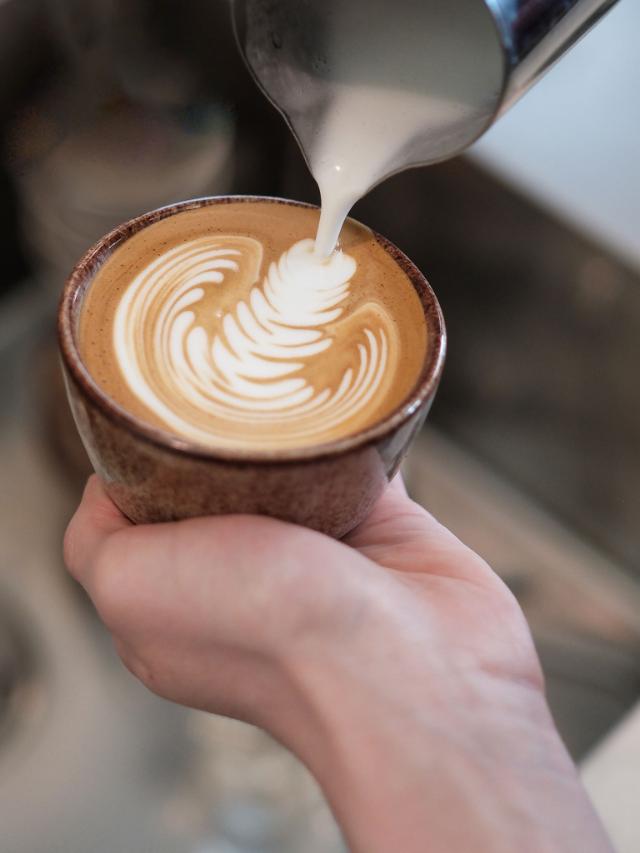 hænder laver latte art mønster i keramisk kaffekop