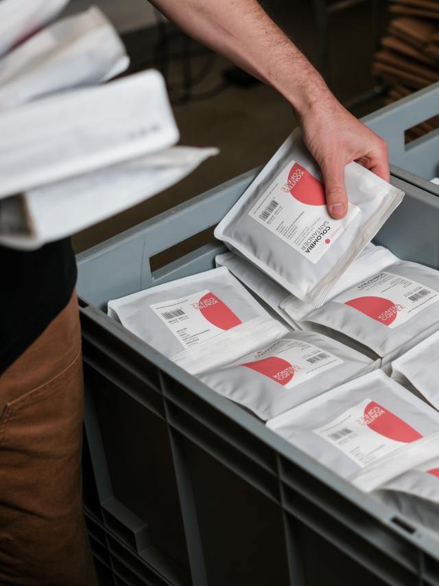 en person pakker kaffeposer med lysristet kaffe i en grå fragtkasse