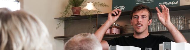 Person står med hænderne over hovedet og forklarer foran et kaffesmagshjul