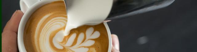 Mælk hældes fra en steamekande ned i en kaffekop i et forsøg på at lave latteart